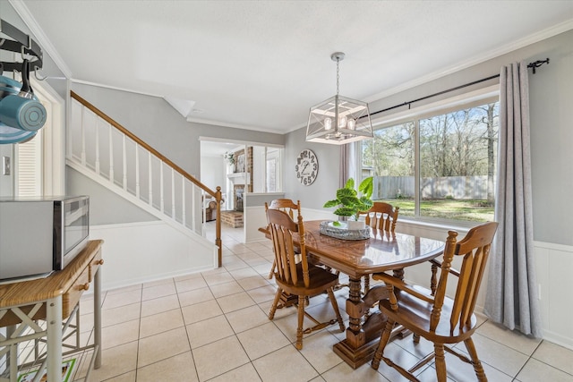 dining area with light tile patterned flooring, a notable chandelier, stairs, ornamental molding, and wainscoting