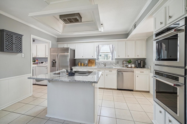 kitchen with stainless steel appliances, washing machine and dryer, light tile patterned flooring, and ornamental molding