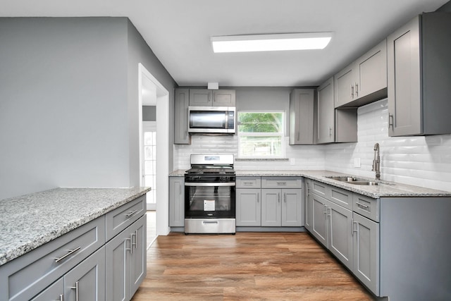 kitchen with sink, light wood-type flooring, stainless steel appliances, and light stone countertops