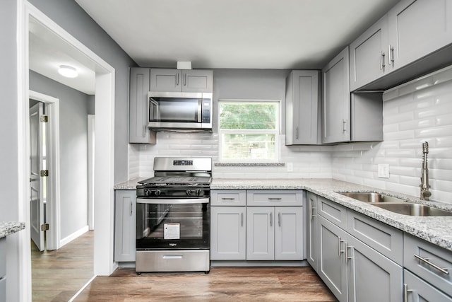 kitchen featuring stainless steel appliances, light stone countertops, sink, and gray cabinets