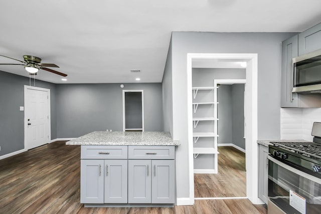 kitchen with dark hardwood / wood-style flooring, gray cabinets, light stone countertops, and appliances with stainless steel finishes