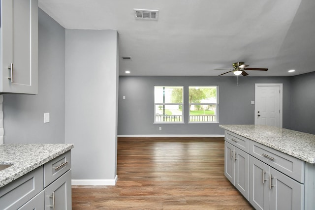 kitchen with light stone countertops, gray cabinetry, ceiling fan, and light hardwood / wood-style flooring