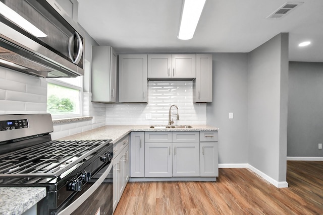 kitchen with sink, gray cabinets, light stone countertops, gas range oven, and light hardwood / wood-style floors