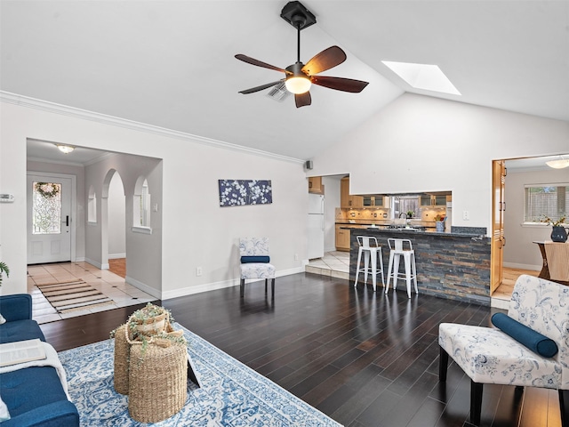 living room featuring visible vents, light wood-style floors, arched walkways, baseboards, and a ceiling fan