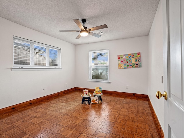 unfurnished room with a textured ceiling, visible vents, a ceiling fan, and baseboards