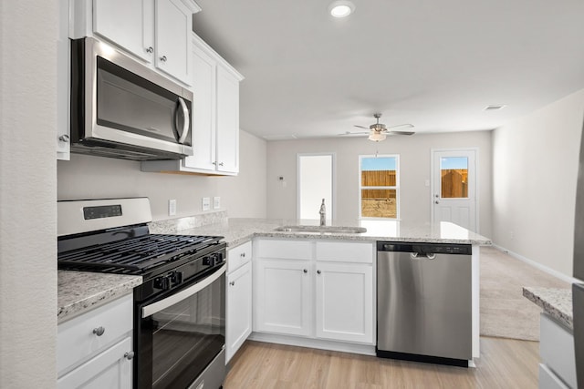 kitchen with appliances with stainless steel finishes, white cabinetry, sink, light stone counters, and kitchen peninsula