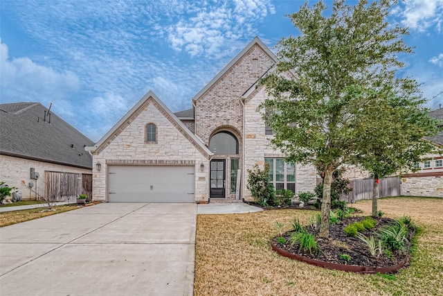 french country home featuring brick siding, concrete driveway, a front yard, fence, and a garage