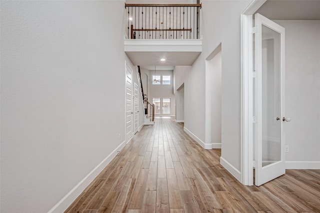 corridor featuring stairs, a high ceiling, baseboards, and wood finished floors