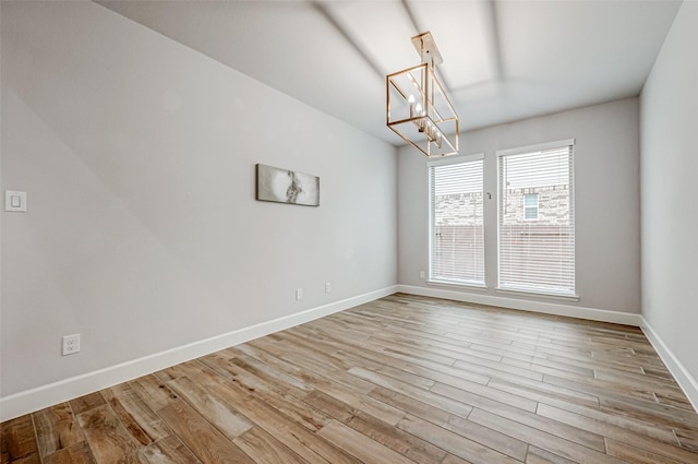 spare room with light wood-style floors, baseboards, and a chandelier