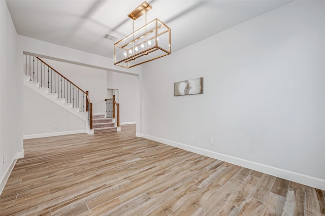 unfurnished room with visible vents, baseboards, stairway, light wood finished floors, and an inviting chandelier