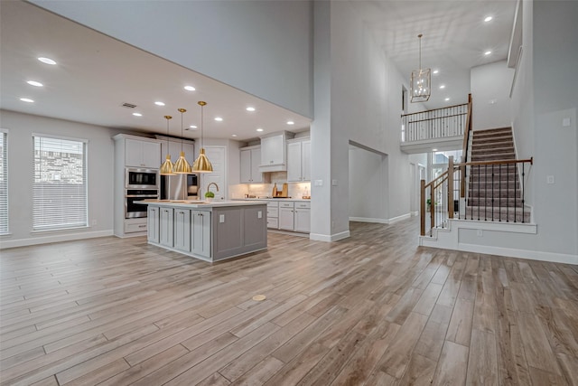 kitchen with a center island with sink, open floor plan, stainless steel appliances, light countertops, and light wood-style floors