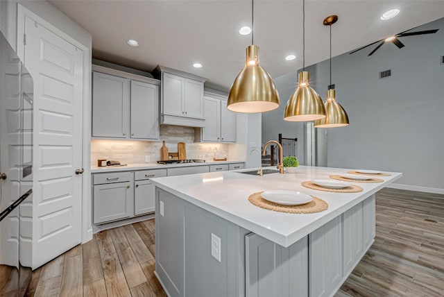 kitchen featuring light wood finished floors, backsplash, light countertops, gas cooktop, and a sink