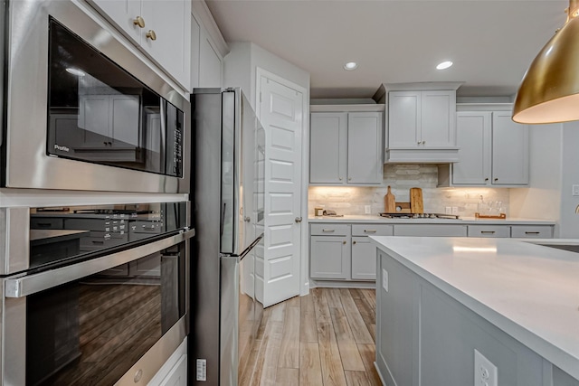 kitchen featuring light wood finished floors, light countertops, backsplash, appliances with stainless steel finishes, and premium range hood