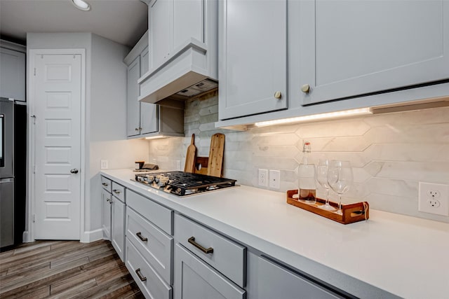 kitchen with tasteful backsplash, light countertops, stainless steel gas stovetop, and wood finished floors