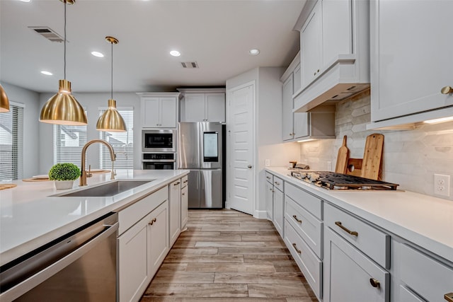 kitchen with appliances with stainless steel finishes, light countertops, a sink, and light wood-style flooring