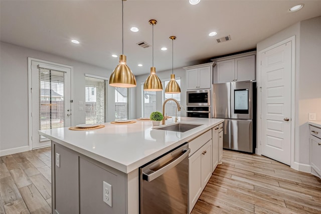 kitchen featuring light wood finished floors, stainless steel appliances, light countertops, visible vents, and a sink