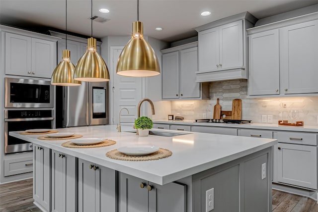 kitchen featuring visible vents, custom range hood, appliances with stainless steel finishes, wood finished floors, and a sink