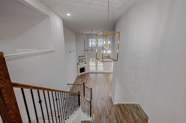 staircase with baseboards, wood finished floors, a fireplace, a notable chandelier, and recessed lighting