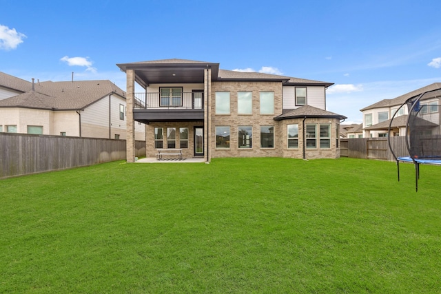 back of property featuring a balcony, a yard, a trampoline, and a patio area