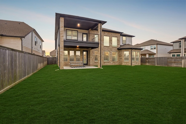 back house at dusk featuring a patio, a balcony, and a lawn