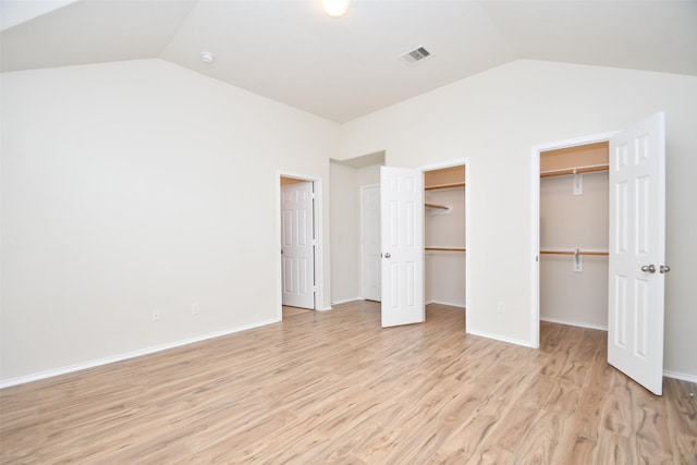 unfurnished bedroom with two closets, vaulted ceiling, and light wood-type flooring