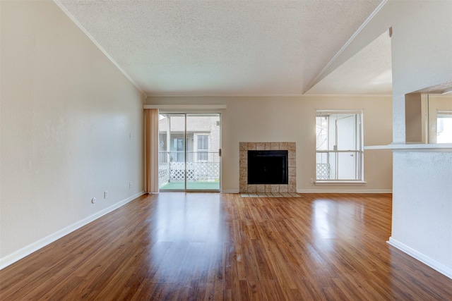 unfurnished living room with wood-type flooring, a tiled fireplace, a textured ceiling, and plenty of natural light