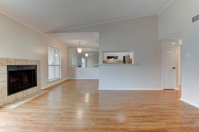 unfurnished living room with crown molding, lofted ceiling, a tiled fireplace, and light hardwood / wood-style floors