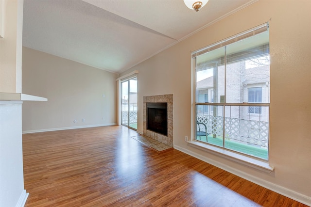 unfurnished living room featuring ornamental molding, plenty of natural light, a tiled fireplace, and hardwood / wood-style floors