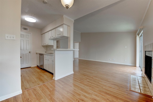 kitchen featuring a tiled fireplace, dishwasher, kitchen peninsula, and white cabinets