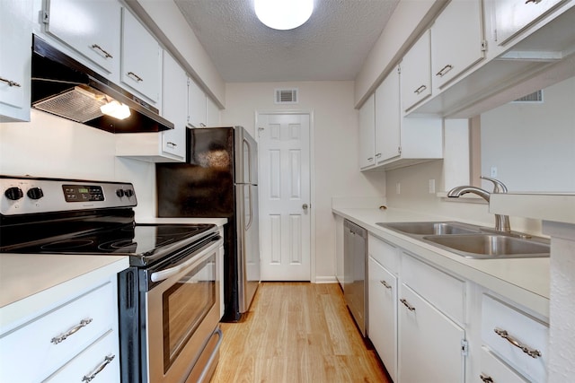 kitchen with appliances with stainless steel finishes, white cabinetry, sink, light hardwood / wood-style floors, and a textured ceiling