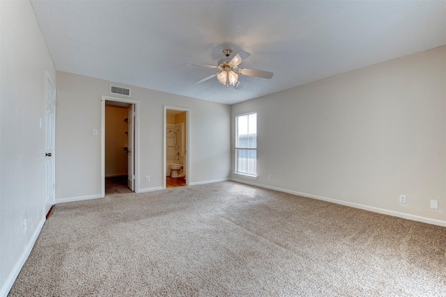 unfurnished bedroom featuring ceiling fan, a spacious closet, ensuite bath, and light carpet