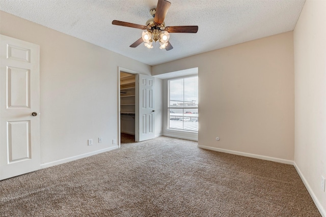 unfurnished bedroom featuring carpet flooring, a spacious closet, ceiling fan, a textured ceiling, and a closet