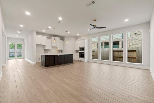 kitchen featuring pendant lighting, light hardwood / wood-style flooring, white cabinetry, tasteful backsplash, and a center island with sink