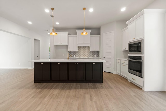 kitchen featuring decorative light fixtures, built in microwave, white cabinets, a kitchen island with sink, and stainless steel oven