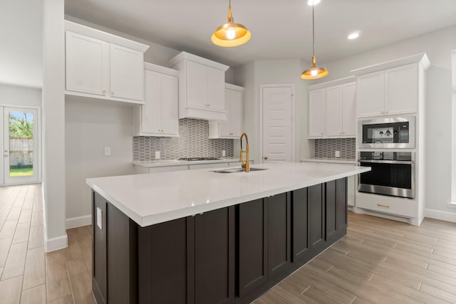 kitchen featuring appliances with stainless steel finishes, white cabinetry, sink, hanging light fixtures, and a kitchen island with sink