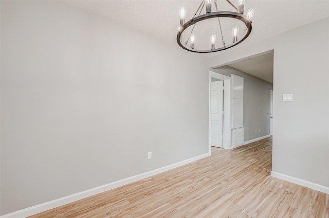 unfurnished room featuring baseboards, a chandelier, and light wood finished floors