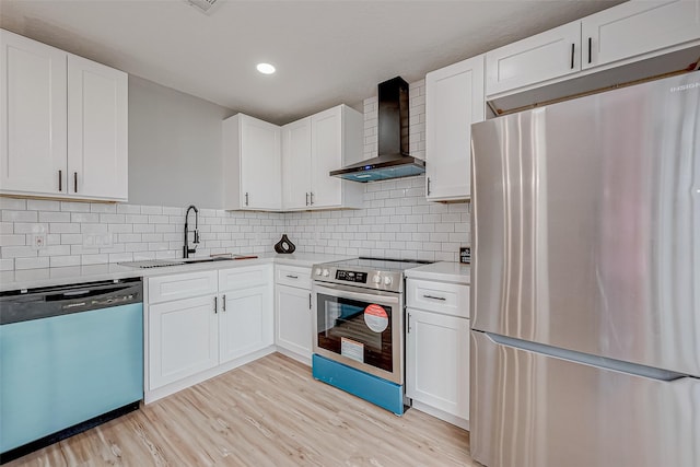 kitchen featuring light wood-type flooring, a sink, wall chimney range hood, stainless steel appliances, and light countertops