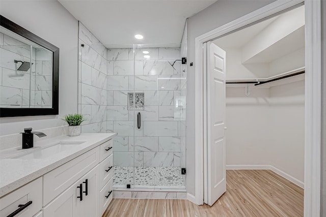 full bathroom with a walk in closet, baseboards, a stall shower, wood finished floors, and vanity