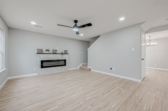 unfurnished living room with ceiling fan with notable chandelier, a fireplace, and light wood-type flooring