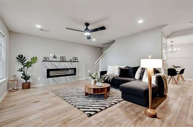 living room with a high end fireplace, visible vents, baseboards, light wood-style flooring, and ceiling fan with notable chandelier