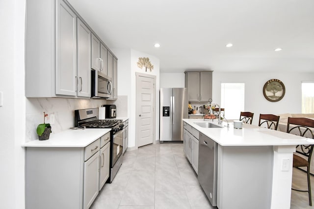 kitchen with stainless steel appliances, a breakfast bar, sink, and gray cabinets