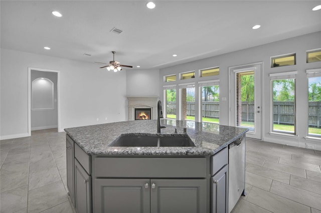 kitchen with dark stone counters, sink, a center island with sink, and gray cabinetry