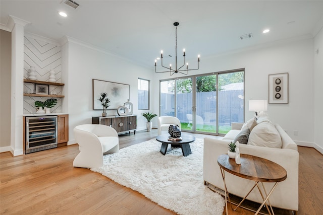 living room featuring wine cooler, a notable chandelier, light hardwood / wood-style flooring, and ornamental molding