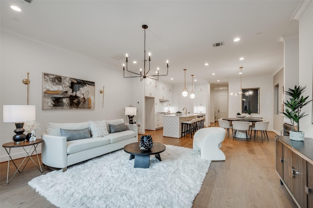 living room with ornamental molding, sink, a notable chandelier, and light hardwood / wood-style floors