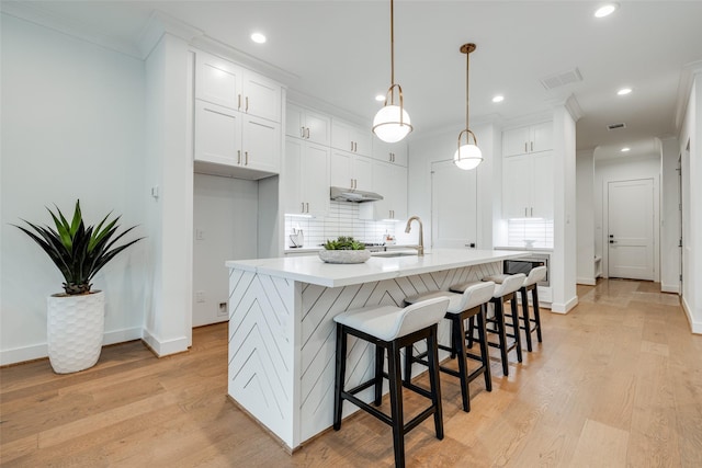 kitchen with sink, decorative backsplash, white cabinets, a center island with sink, and decorative light fixtures