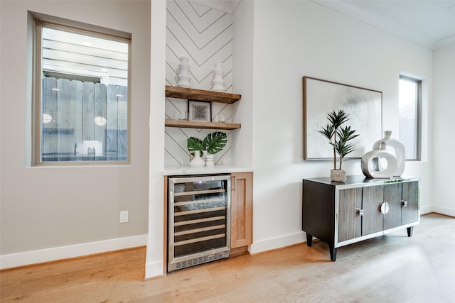 bar featuring wine cooler, ornamental molding, and light wood-type flooring