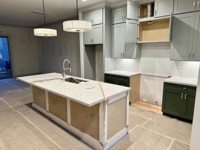 kitchen featuring sink, a kitchen island with sink, hanging light fixtures, light stone counters, and decorative backsplash