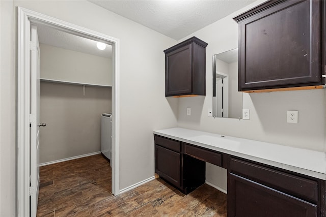 unfurnished office with dark wood-style floors, built in study area, a textured ceiling, washer / dryer, and baseboards