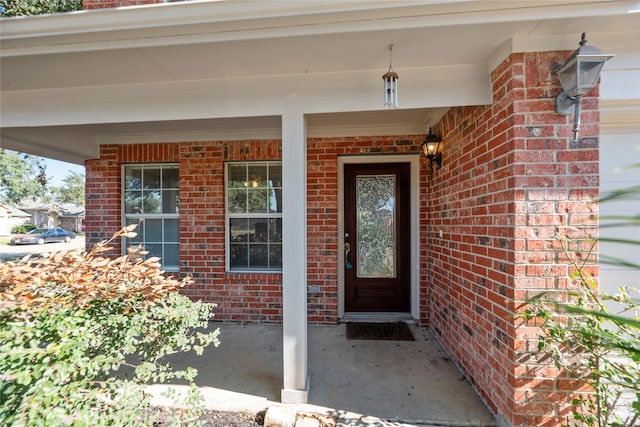 view of exterior entry with a porch and brick siding