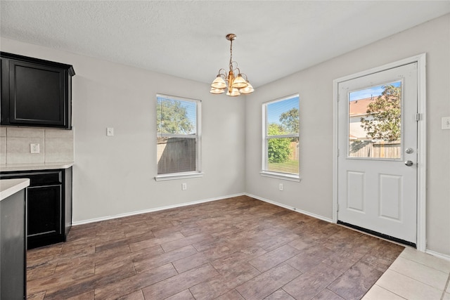 unfurnished dining area with a notable chandelier, a textured ceiling, baseboards, and wood finished floors